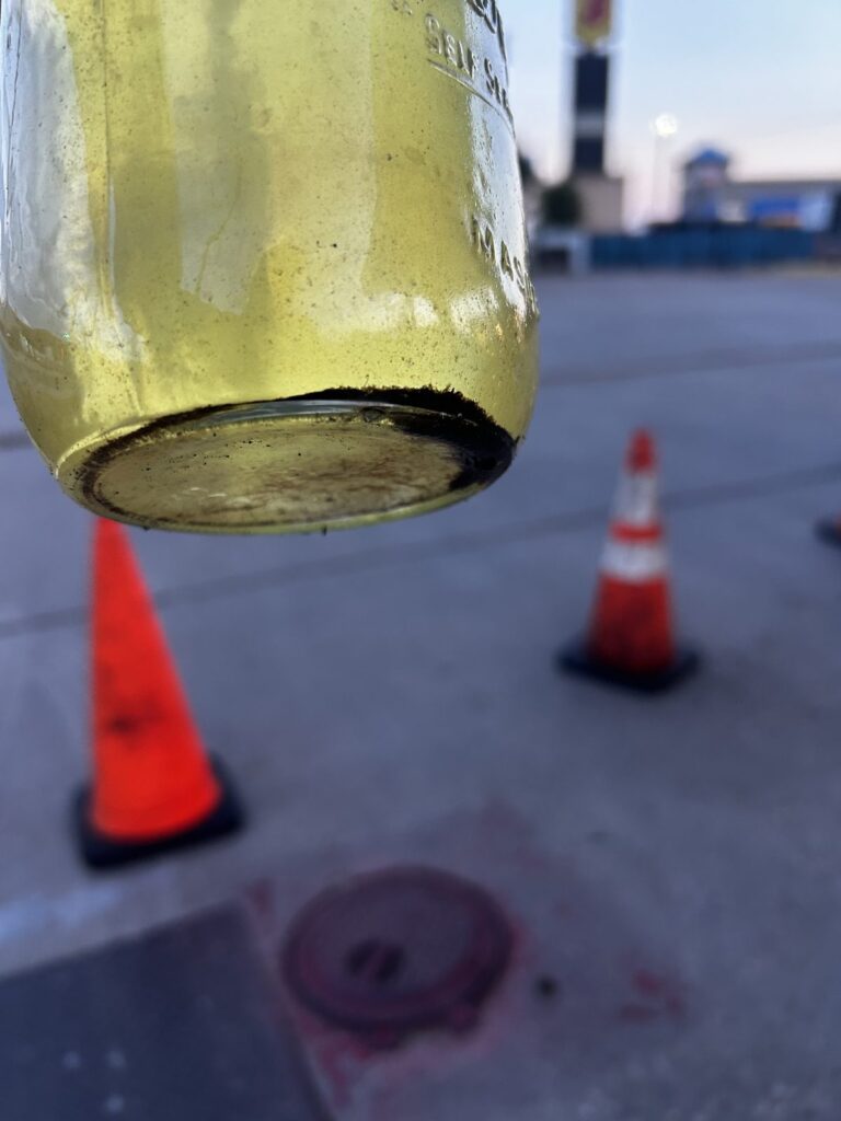 A jar of fuel with dark sediment settled along the bottom