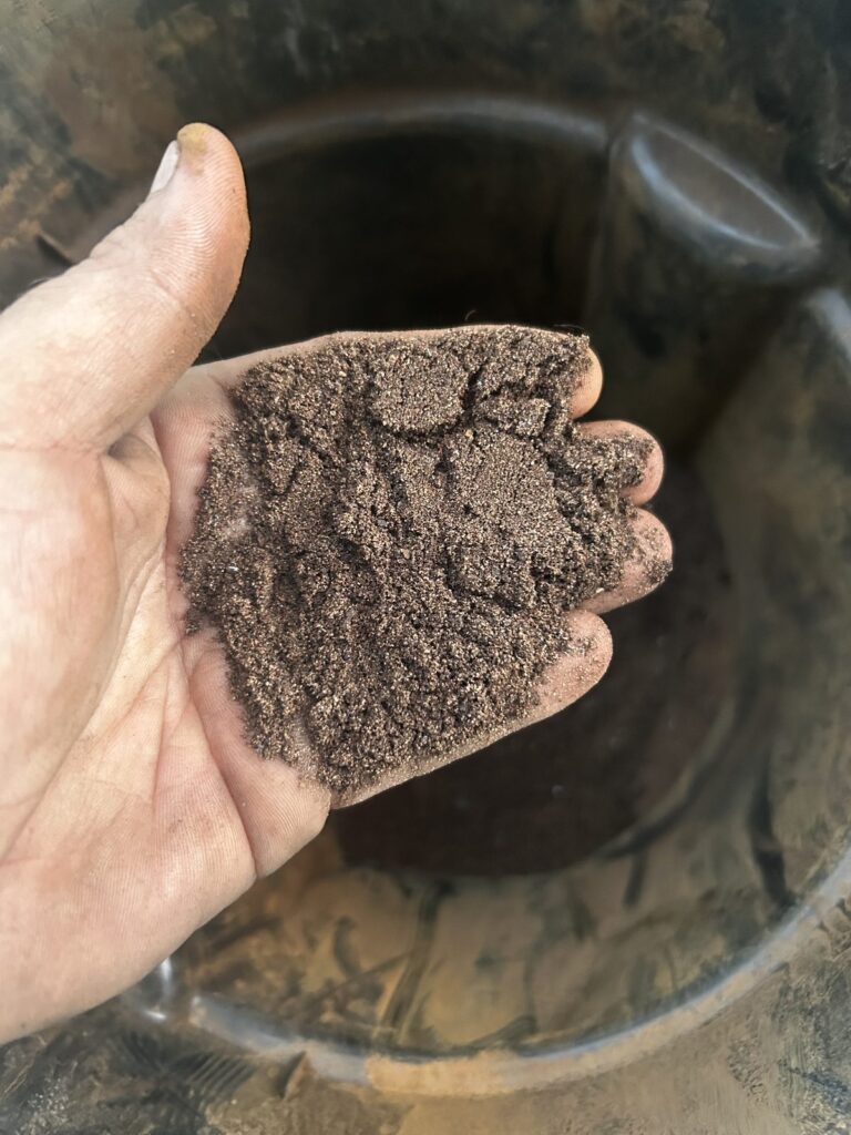 A handful of fine brown sediment held over an open tank