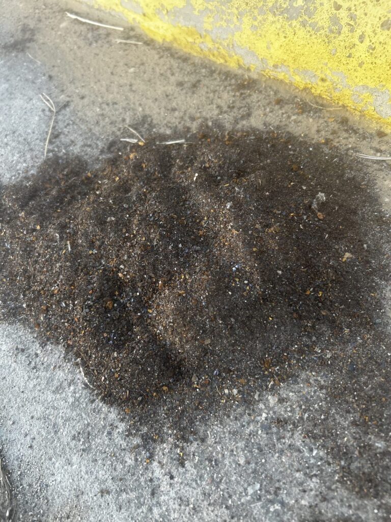 A pile of dark grit on the concrete next to a yellow line